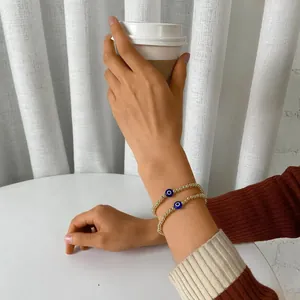 Detail of two-piece gold beaded elastic bracelets featuring evil eye charms on model