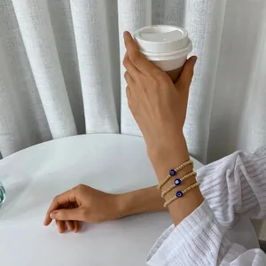 Detailed view of three-piece gold bead bracelets with blue evil eye charms on wrist