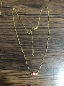 Detailed close-up of gold stainless steel necklace with red enamel evil eye pendant
