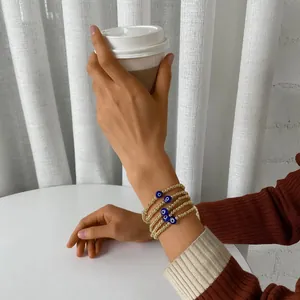 Detailed view of layered gold evil eye bead bracelets worn by a model holding a cup