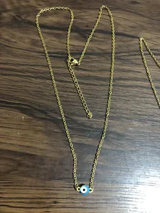 Detail of gold-plated evil eye necklace with lobster clasp on wood surface
