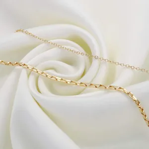 Macro detail of 18K gold-plated stainless steel chains on soft white silk fabric
