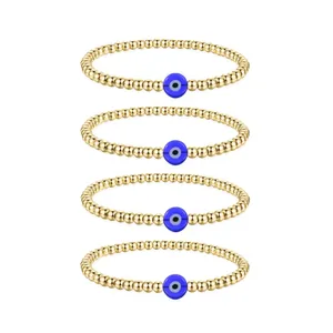 Detailed view of four golden bead bracelets with blue evil eye charms on white background