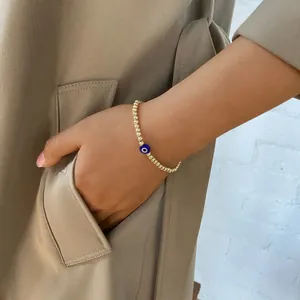 Close-up of gold beaded Evil Eye bracelet worn with a minimalist beige trench coat