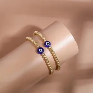Detailed view of two gold beaded bracelets featuring blue evil eye charms on a stand