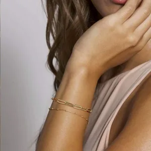 Detail of layered gold paperclip and bead chain bracelets on a woman's wrist