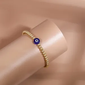Detailed close-up of golden beaded bracelet with blue evil eye charm on wrist stand