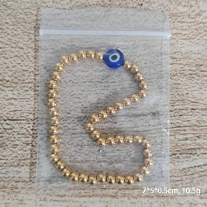 Golden stainless steel beaded bracelet featuring a blue evil eye charm on wooden background