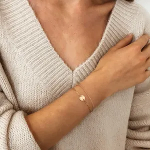 Detail of 18K gold-plated double-layer bracelet with hammered disk pendant on knit fabric