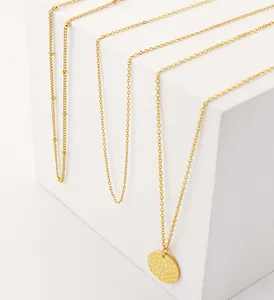 Detail of layered gold stainless steel necklaces with a hammered disc pendant on white cubes