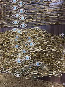 Detail van gouden paperclip-armbanden met blauwe boze oog hangers en zirkonia-accenten