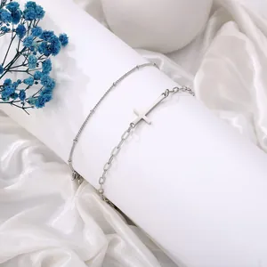 Detail van zilveren dubbele roestvrijstalen armband met kruis en kralen op fluweel