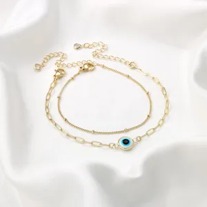 Detail van 18K gouden armbanden met evil eye bedeltje op een zachte witte satijnen ondergrond