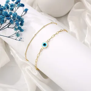 Detail van gouden evil eye armband op witte zijde met parels en 18K vergulde afwerking