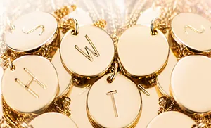 Macro detail of polished 18K gold paperclip necklaces with engraved initial pendants