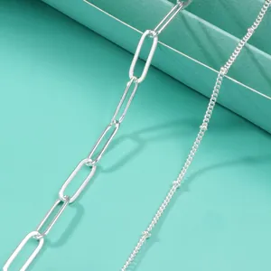 Detail van een dubbellaagse roestvrijstalen armband met paperclip- en fijne schakelketting