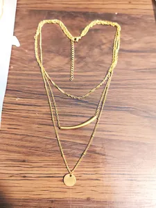 Detail of gold multilayered necklace with curved tube and round coin charms on wood