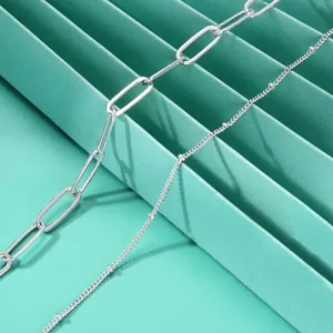 Detail van zilveren dubbele ketting met paperclip-schakels en subtiele kraalaccenten