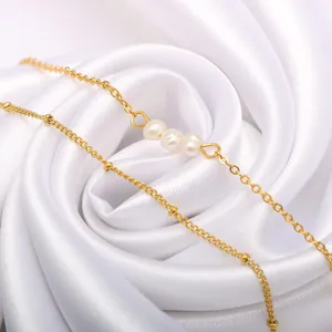 Elegante dubbellaagse gouden kettingarmband met 6 mm witte parels op witte zijden achtergrond