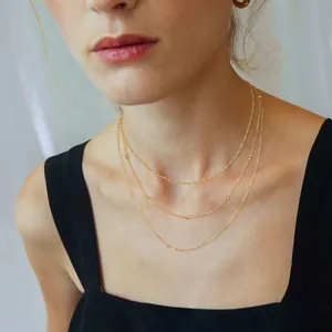Close-up of triple-layered gold necklaces with delicate beads on a square neck top