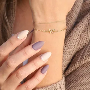 Detailweergave van een gouden paperclip-armband met vlinderbedel op de pols van model