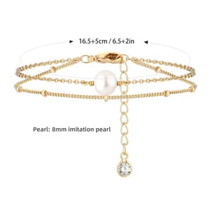 Detail van een gelaagde gouden armband met parel, paperclipketting en karabijnslot