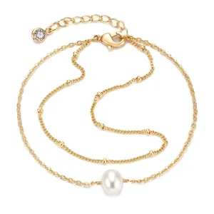 Detail van dubbellaagse gouden kettingarmband met druppelparel en zirkoonbedel