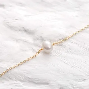 Detailopname van een 18K vergulde kettingarmband met een enkele witte parel