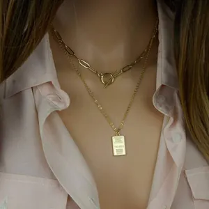 Close-up of layered 18K gold paperclip chain necklace with OT toggle and gold bar pendant