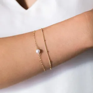 Detail van de dubbellaagse gouden kettingarmband met 8mm parel op de pols van een model