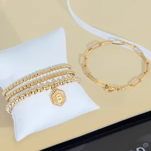 Détail de bracelets perlés plaqués or 18K et chaîne avec pendentif lettre B hexagone