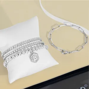 Vue détaillée du lot de bracelets argentés à perles avec pendentif B sur coussin blanc