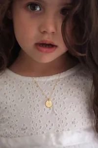 Detailed close-up of a 18K gold letter A pendant necklace on a child's neck