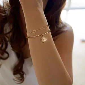 Detail van een dubbellaagse gouden paperclip en kralenketting armband met letter M hanger
