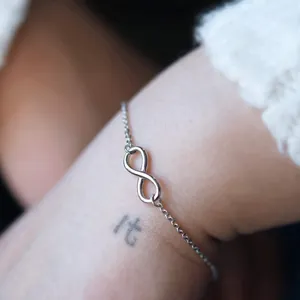 Macro shot of silver infinity symbol charm on a delicate stainless steel chain bracelet