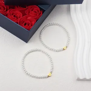 Detail of two white pearl bracelets with golden heart charms engraved with letters M and K