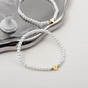 Macro detail of faux pearl bracelets with 18K gold heart pendants featuring M and K engravings