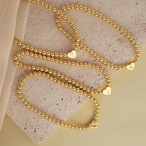 Close-up of 18K gold-plated beaded bracelets with engraved heart-shaped alphabet charms