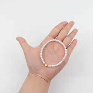 Detail of beaded pearl bracelet with gold heart charm engraved with the letter A