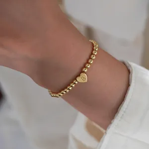 Close-up of gold beaded bracelet featuring a heart pendant with an engraved letter B