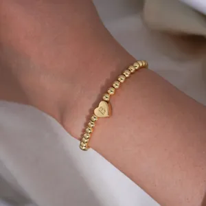 Macro detail of gold-plated beaded bracelet with a polished heart charm engraved with letter B