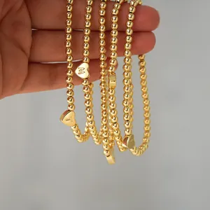 Macro detail of 18K gold-plated beaded bracelets featuring engraved heart letter charms