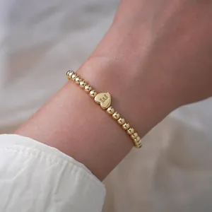 Close-up of gold beaded stretch bracelet featuring a heart pendant with engraved letter E