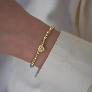 Detailed close-up of 18K gold-plated beaded bracelet featuring a heart initial E charm