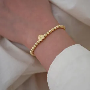 Detail of 18K gold-plated beaded bracelet with a heart-shaped letter E charm