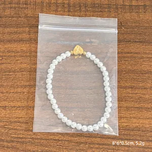 Faux pearl bracelet with 18K gold heart pendant featuring engraved letter X on wood background