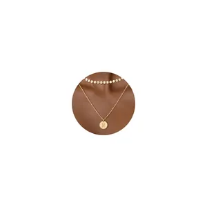 Detalle del collar de capas de oro de 18K con lentejuelas y colgante con la letra N grabada