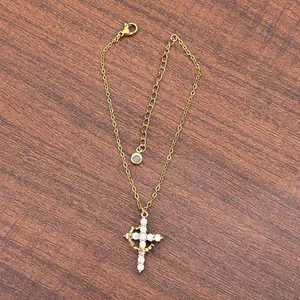 Detail of 18K gold double-layer necklace with crystal cross pendant on wood surface