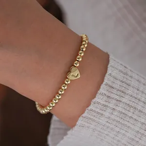 Macro shot of 18K gold-plated beaded bracelet featuring a heart pendant engraved with letter L
