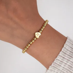 Detailed macro view of an 18K gold plated beaded bracelet featuring an engraved heart pendant